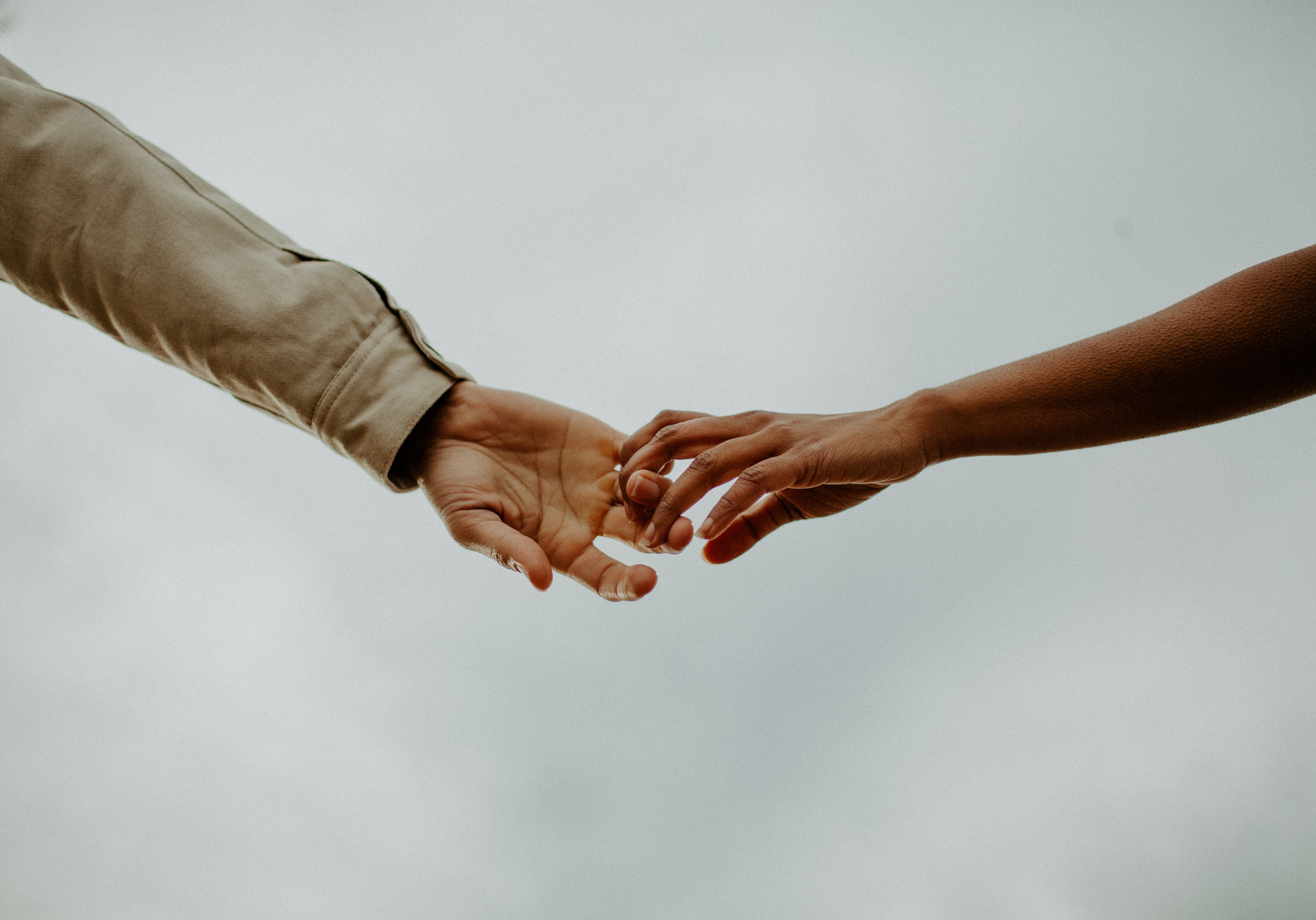 MIDSECTION OF COUPLE HOLDING HANDS AGAINST SKY DURING WINTER
